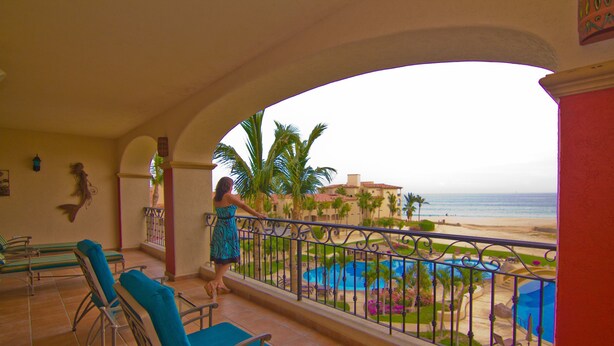 Un balcon avec vue sur une plage, une piscine et des palmiers.