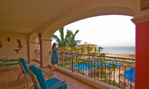 A balcony with a view of a beach, pool, and palm trees.