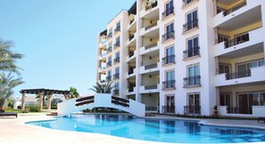 Un hotel de varios pisos con balcones, piscina y un espacio al aire libre cubierto con palmeras.