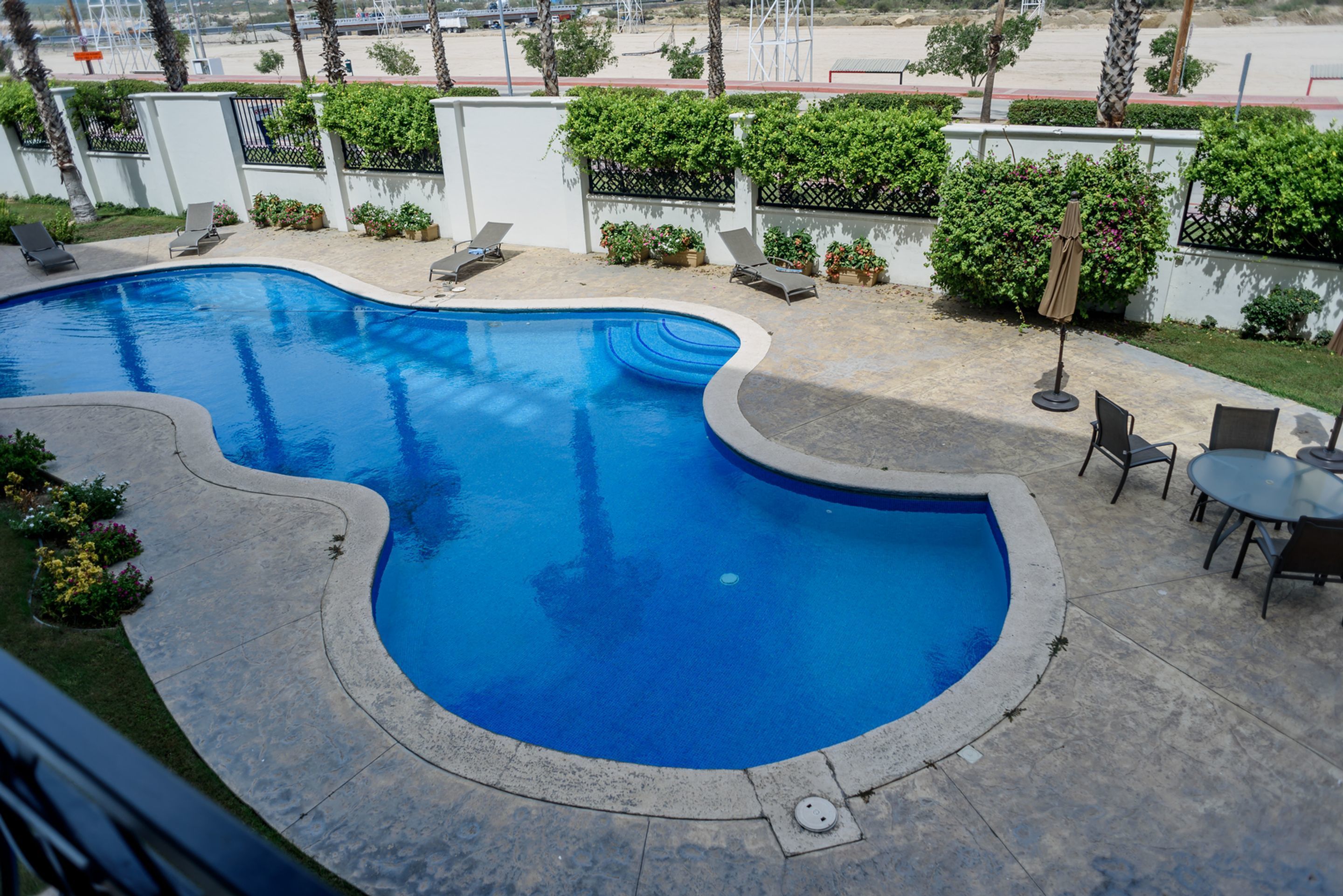 A swimming pool with a curved edge, surrounded by lounge chairs and a small table with an umbrella.