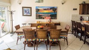 A dining area with a large table, wicker chairs, and a painting of a sunset. - Las Olas A104 3 BR by Casago (San José del Cabo)