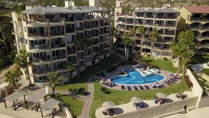 A multi-story hotel with balconies, a central swimming pool, and surrounding palm trees. - Las Olas A104 3 BR by Casago (San José del Cabo)