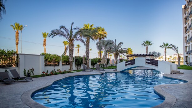 A swimming pool surrounded by palm trees and lounge chairs. - Puerta Cabos Village G207 2BR by Casago (Cabo San Lucas)