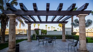 An outdoor patio with a pergola, stone columns, and seating area. - Puerta Cabos Village G207 2BR by Casago (Cabo San Lucas)
