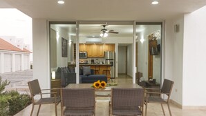 A modern dining area with a glass partition, a ceiling fan, and a view into a kitchen and living room. - Peninsula 106 2 BR by Casago (San José del Cabo)