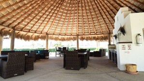 A covered outdoor seating area with wicker furniture and a thatched roof. - Peninsula 106 2 BR by Casago (San José del Cabo)