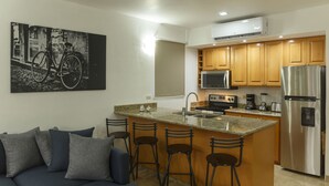 A modern kitchen with a central island, bar stools, a refrigerator, and a microwave. - Peninsula 106 2 BR by Casago (San José del Cabo)