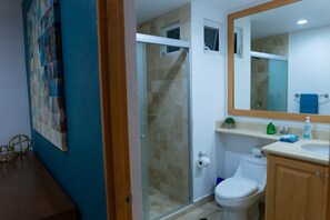 Een badkamer met een douchecabine van glas, een toilet, een wastafel met spiegel en een wandplank met toiletartikelen.