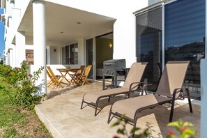 Een overdekt buitengebied met lounge stoelen, een eettafel en een barbecue.
