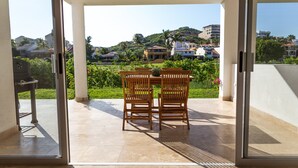 Un patio abierto con una mesa, sillas, una parrilla y vistas a una colina con edificios.