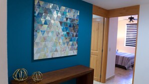 Una habitación con pared azul, un banco de madera y una obra de arte geométrica.