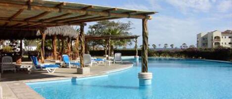 Un espace piscine avec des chaises longues et une structure recouverte d’un toit de chaume.
