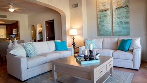 A living room with two sofas, a coffee table, and a lamp. There is a kitchen in the background. - Las Mananitas C308 3 BR by Casago (San José del Cabo)