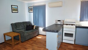 A compact living space with a kitchenette, a grey sofa, a small table, and a window with curtains. - 10 Tautog Street - Great Family space in central location (EXMOUTH)