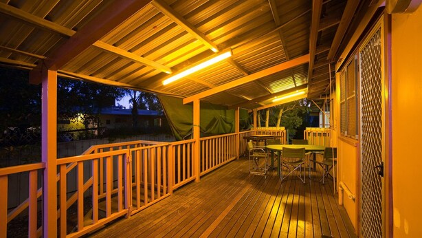 An outdoor wooden deck with a railing, tables, and chairs, under a covered area with overhead lighting. - 10 Tautog Street - Great Family space in central location (EXMOUTH)