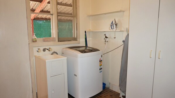 A compact laundry room with a washing machine, a sink, and a drying rack.
