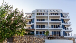 Un hotel de varios pisos con balcones, fachada de piedra y un gran árbol en primer plano.