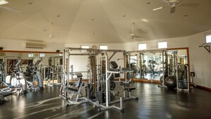 Un gimnasio con equipo de ejercicio diverso, un ventilador de techo y ventanas amplias.