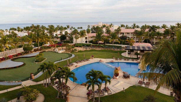 Un resort con una piscina grande, palmeras y vistas al océano.