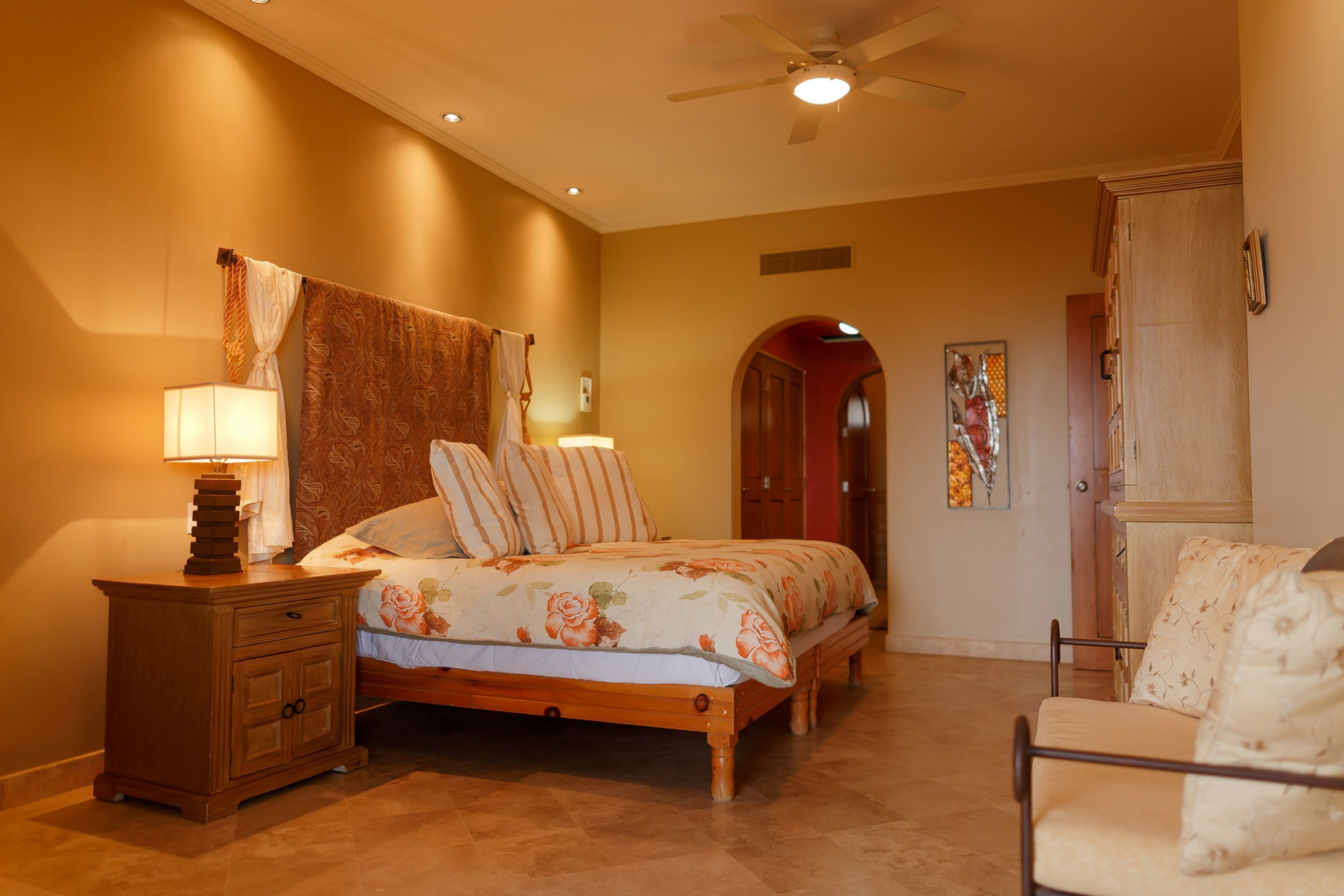 A bedroom with a bed, nightstand, chair, and a ceiling fan.