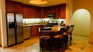 Una cocina con armarios de madera, un refrigerador de acero inoxidable, un microondas y una estufa. Hay una zona de comedor con una mesa y sillas.