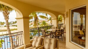 A balcony with wicker furniture, a pool, and palm trees. - Las Mananitas E3301 2 BR by Casago (San José del Cabo)