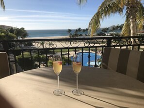 Ein Balkon mit zwei Gläsern eines hellen Getränks, Blick auf Pool und Strand.