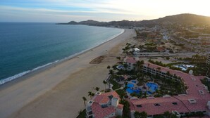 An aerial view of a coastal resort with a beach, swimming pools, and a mountainous backdrop. - Las Mananitas E3301 2 BR by Casago (San José del Cabo)