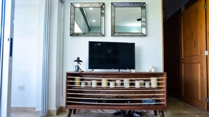 A room with a TV on a wooden stand, two mirrors on the wall, and a door to the right. - Peninsula 103 2 BR by Casago (San José del Cabo)