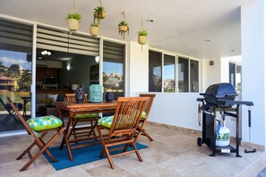 Un patio al aire libre con mesa y sillas de madera, una parrilla y jardineras colgantes.