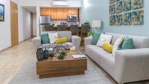 A modern living room with a grey sofa, a wooden coffee table, and a kitchen in the background. - Peninsula 103 2 BR by Casago (San José del Cabo)