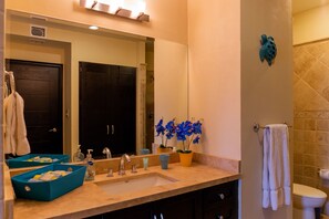 Une salle de bain comprenant un lavabo, un miroir, deux serviettes, une plante en pot et un espace douche.