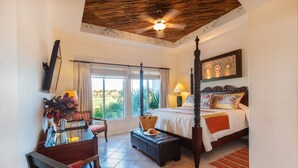 A spacious bedroom with a large bed, a sitting area with a chair and table, and a ceiling fan. - Villa De Oro 106 3 BR by Casago (Cabo San Lucas)