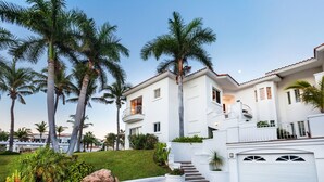 A white two-story house with a white garage, surrounded by palm trees and a well-maintained lawn. - Villa De Oro 106 3 BR by Casago (Cabo San Lucas)