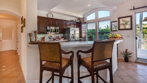 A kitchen with dark wooden cabinets, a stainless steel refrigerator, and a large island with two chairs. - Villa De Oro 106 3 BR by Casago (Cabo San Lucas)