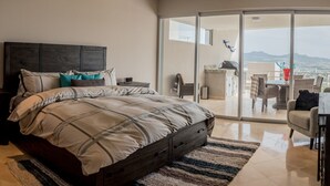 A bedroom with a bed, a dresser, a desk, and a balcony with a view. - Cascadas de Pedregal 711 3 BR by Casago (Cabo San Lucas)