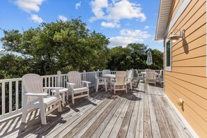Een houten terras met witte Adirondack-stoelen en tafels, omringd door een witte balustrade.