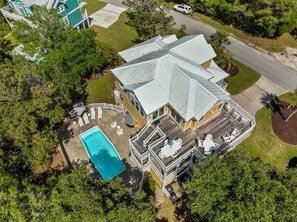 An aerial view of a large house with a swimming pool, multiple decks, and a well-maintained lawn.