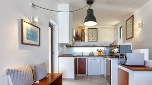 Een kleine keuken met een bankje, een koelkast, een magnetron en een hanglamp.