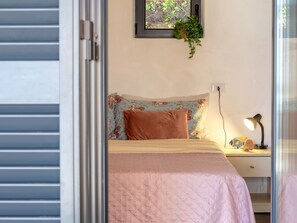 A bedroom with a bed, a bedside lamp, a nightstand, a window with a plant, and a door.