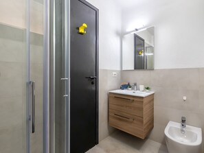 A modern bathroom with a black door, a wooden vanity, a white sink, a bidet, and a mirror above the vanity.
