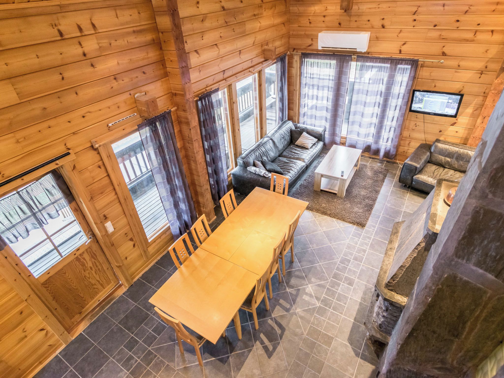 Interior de una cabaña de madera con comedor, sofá y televisor.