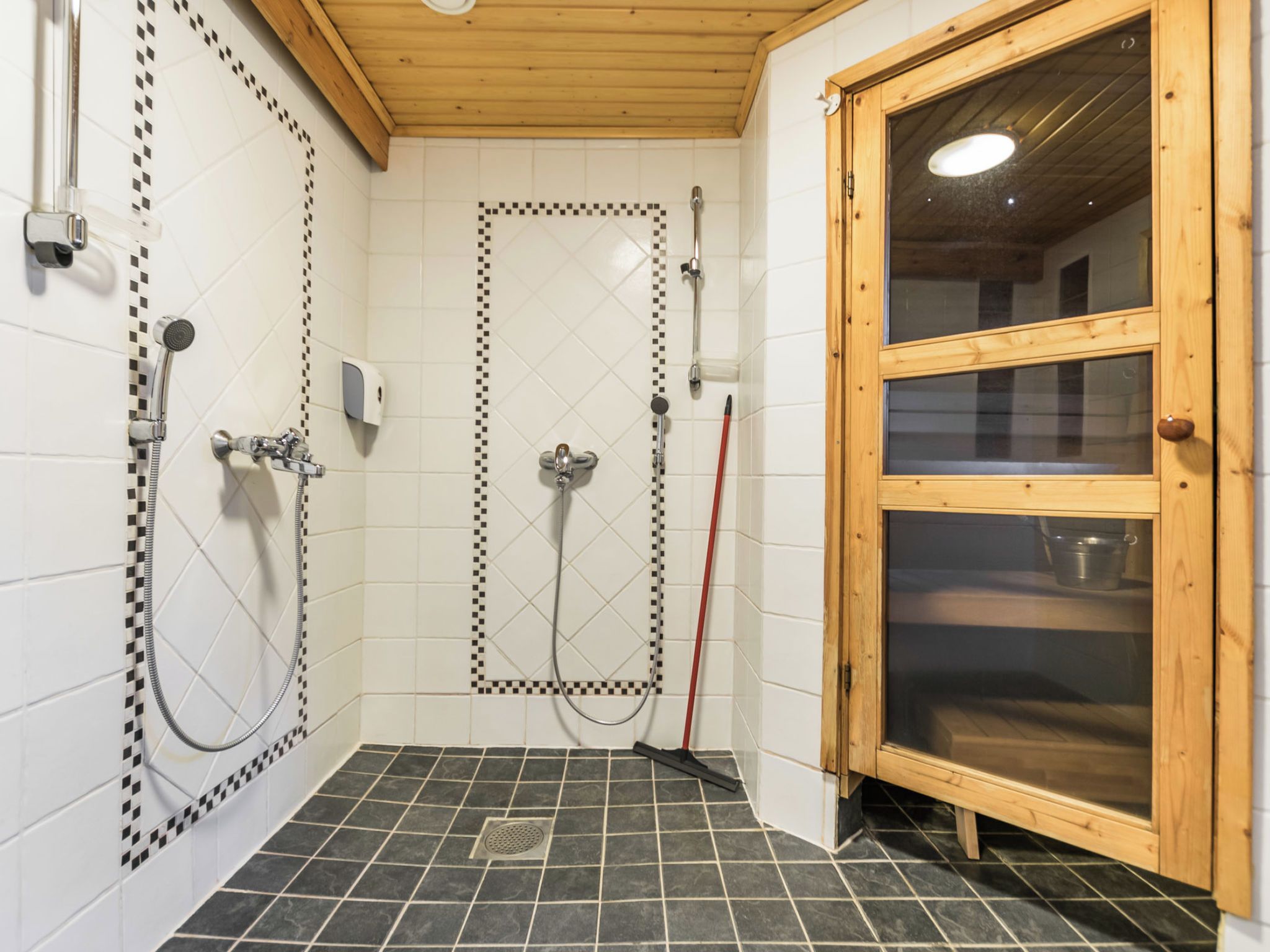 A shower area with a tiled floor, a wooden door, and a showerhead.