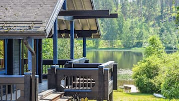 A cabin with a deck overlooking a lake, surrounded by forest.