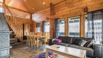 A wooden interior with a staircase, a dining area, and a living room with a sofa and a coffee table.