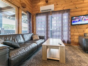 A wooden-paneled room with a leather sofa, a wooden coffee table, and a television on the wall. - Nuppulanranta 14 by Interhome (Kuhmoinen)