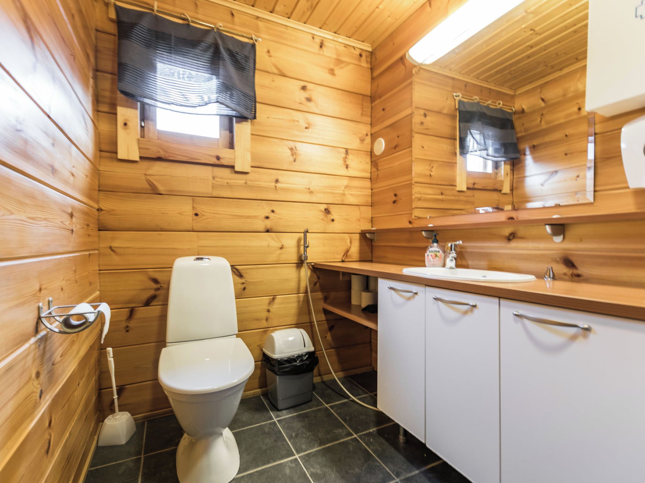 Casa de banho rústica estilo cabana, com sanita, lavatório e armários.