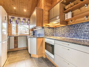 Una cocina con salpicadero de azulejos, armarios de madera, horno empotrado y ventana con vista a una casa.