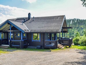 Una cabaña con un porche cubierto, un letrero que indica un número de habitación y vistas a un área boscosa.