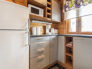 A kitchen with a refrigerator, microwave, coffee maker, and wooden cabinets. - Nuppulanranta 14 by Interhome (Kuhmoinen)